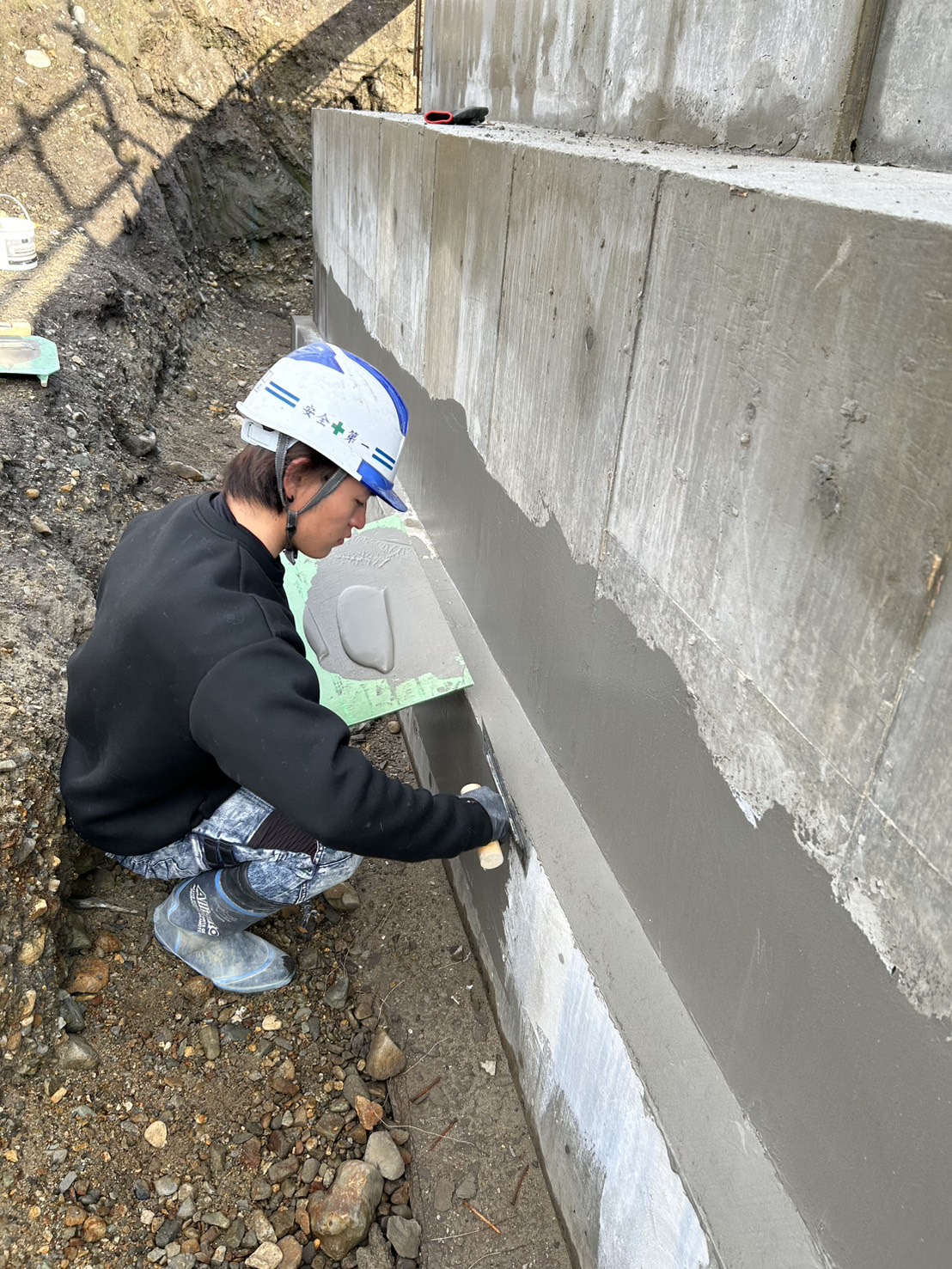 打ちっぱなしのコンクリート壁に左官を施し滑らかに仕上げる職人